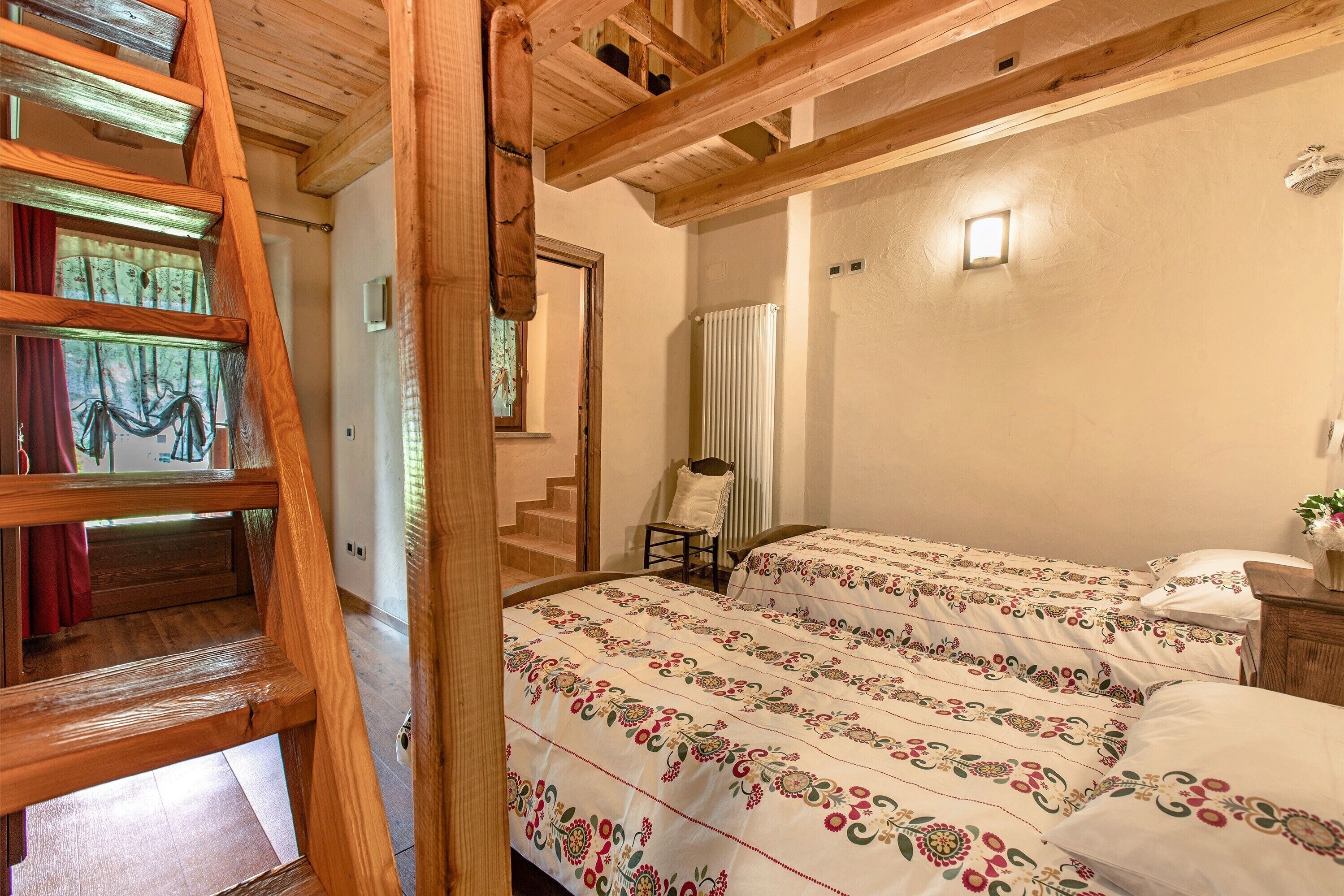 A wooden staircase leading to a bedroom with a bed, a chair, and a small window.