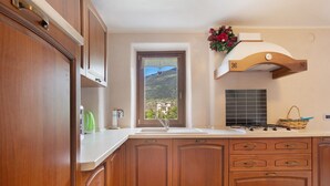 Une cuisine avec des meubles en bois, un plan de travail blanc, une fenêtre donnant sur une montagne et un arrangement floral décoratif.