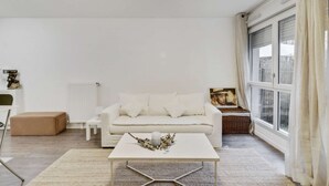 Uma sala de estar minimalista com um sofá branco, uma mesa de centro e uma janela grande com cortinas.