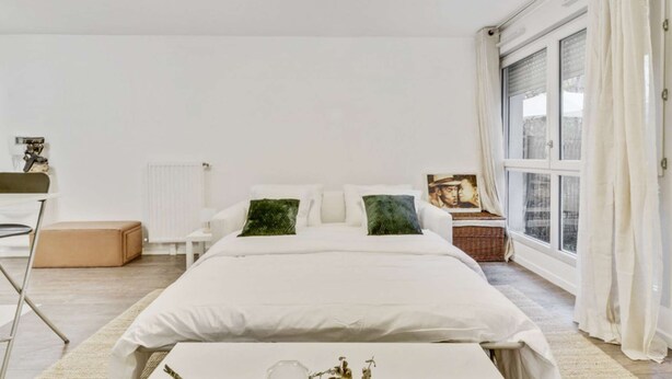 Quarto moderno com uma cama grande, uma mesinha de cabeceira, um radiador e uma janela com cortinas.