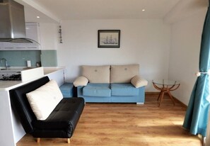 A compact living space with a kitchenette, a blue sofa, a black sofa, and a small round table.