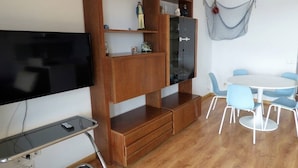 A room with a TV, wooden shelving, a dining table with chairs, and a hammock.