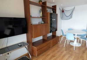 A room with a TV, wooden shelving, a dining table with chairs, and a hammock.