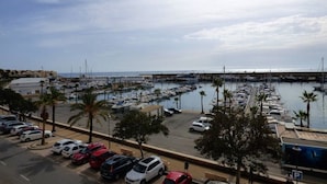 A marina with boats docked, a parking area with cars, and a clear sky.