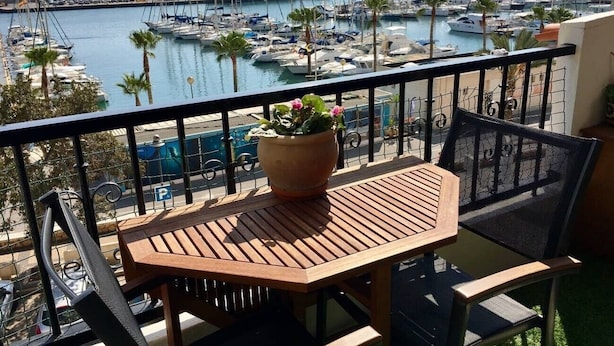 A balcony with a wooden table and chairs, a potted plant, and a view of a marina with boats.