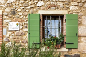 Un bâtiment en pierre avec une enseigne indiquant « AZIENDA AGRITURISTICA LE CAMPAGNOLE », une fenêtre avec des volets verts et des plantes en pot.