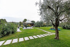 Un jardin agrémenté d’un belvédère, d’un chemin de pierres et d’un grand arbre.