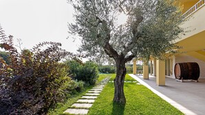 Un sentier bordé d’arbres et ponctué de pierres plates, qui mène à un bâtiment orné d’une tonneau et dont la façade est jaune.