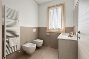 A bathroom with a white radiator, bidet, sink, and a window with curtains.