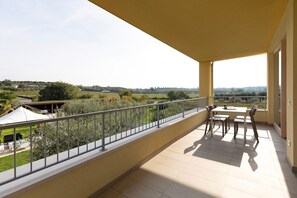 A balcony with a view of a green landscape, a table with chairs, and a white tent.