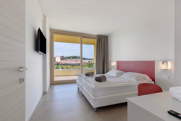 A hotel room with a bed, a desk, a TV, and a sliding glass door to the outside.