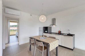 A modern kitchen with a dining table, chairs, a hanging light fixture, and a view through an open door.