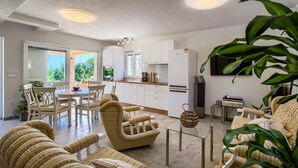 A modern kitchen with white cabinets, a built-in oven, and a refrigerator. There is a dining area with wicker chairs and a glass table. - Gorgeous home in Ugljan (Ugljan)