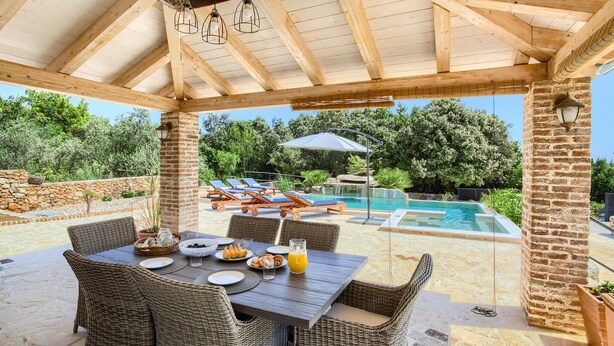 A covered outdoor dining area with wicker furniture, a pool, and a stone wall. - Gorgeous home in Ugljan (Ugljan)