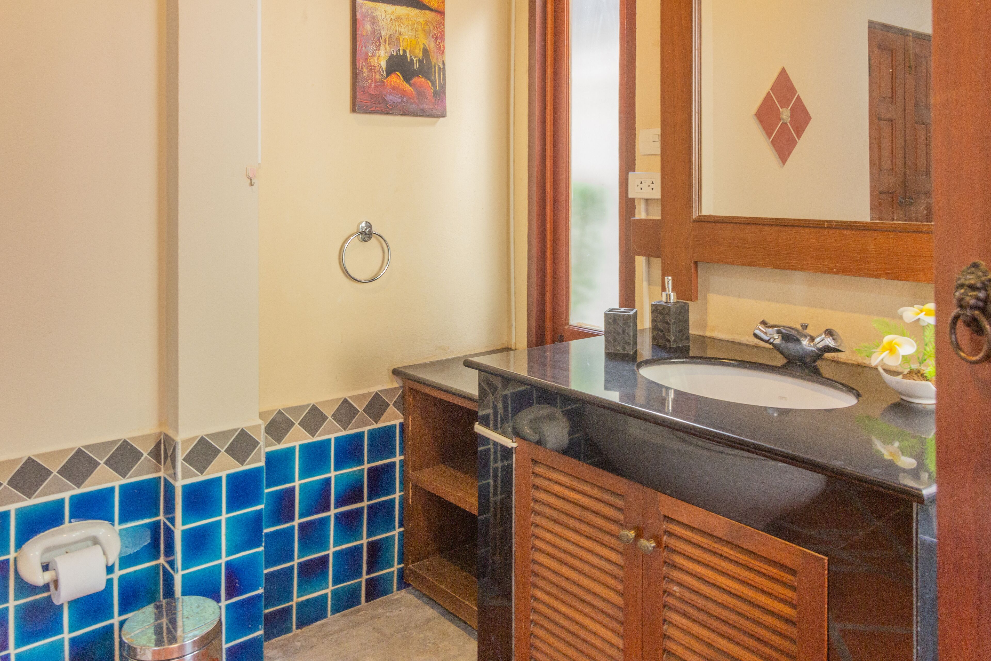 A bathroom with a black sink, wooden cabinets, a mirror, and blue-tiled walls.