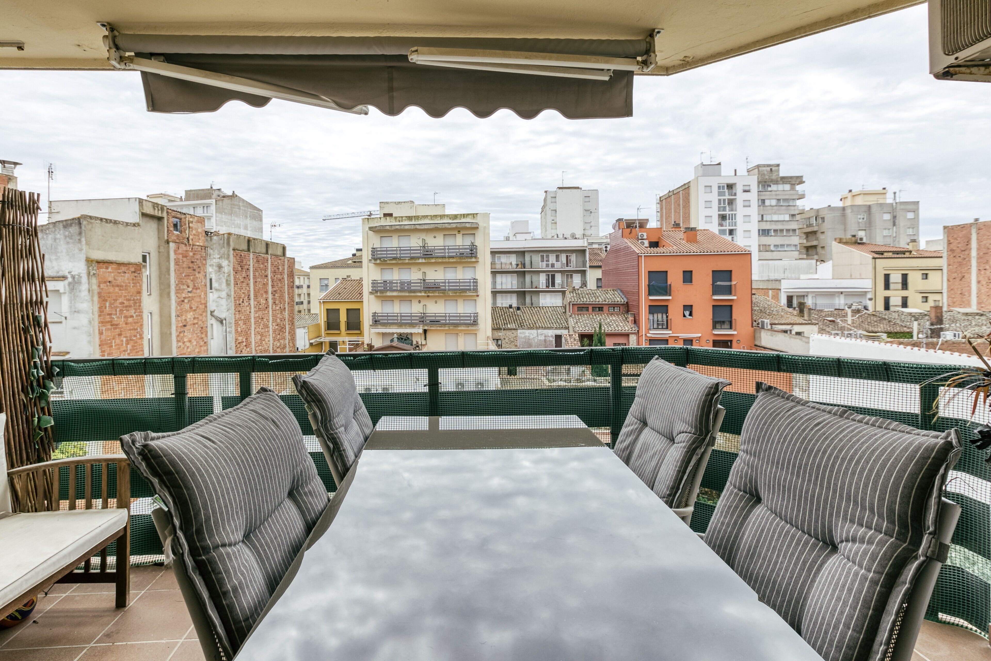 A rooftop terrace with a table and chairs, a green safety net, and a cityscape view.