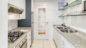 A compact kitchen with a gas stove, double sink, and a door with frosted glass panels. - Apartment 'Calonge Beach' with Private Terrace, Balcony and Air Conditioning (St Antoni de Calonge)