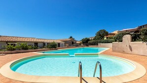 A swimming pool with two metal ladders, surrounded by a tiled deck and a low wall. - Holiday Home "Nuages" with Shared Pool and Private Terrace (Badesi)