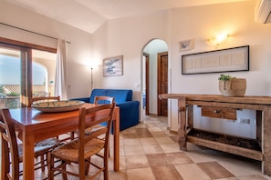 A dining area with a wooden table and chairs, a blue sofa, and a wooden console table with a basket. - Holiday Home "Nuages" with Shared Pool and Private Terrace (Badesi)