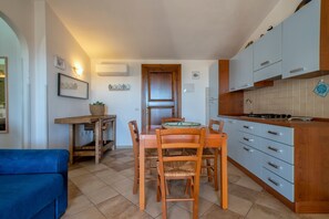 A compact kitchen with a dining table and chairs, a blue sofa, and a wooden cabinet with drawers. - Holiday Home "Nuages" with Shared Pool and Private Terrace (Badesi)