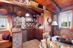 A rustic kitchen with wooden cabinets, a stone wall, a dining area with a table set for two, and a view of greenery outside. - Holiday Home 'Casa El Retiro' with Sea View, Wi-Fi and Air Conditioning (Tijarafe)
