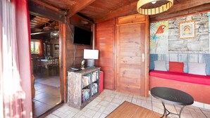 Ein Holzinnenraum mit Fernseher, Bücherregal, einem roten Sofa und einer Steinwand mit Wandgemälde.