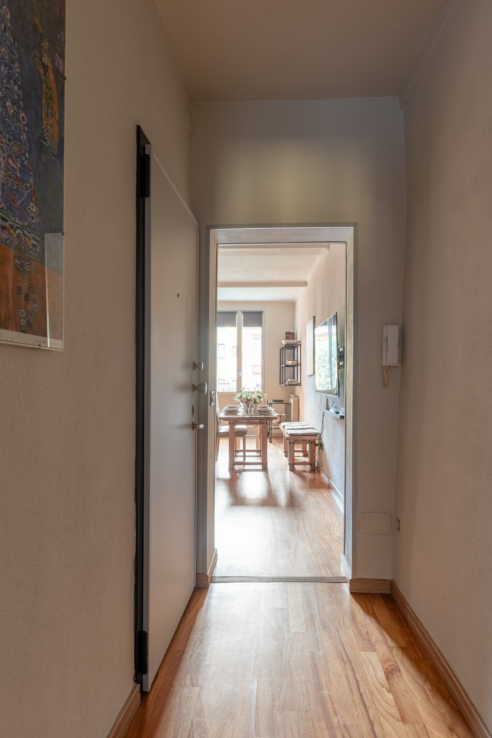 Un pasillo que conduce a un comedor con suelo de madera, una puerta a la izquierda y un aplique en la pared.
