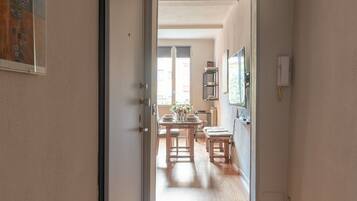 Un pasillo que conduce a un comedor con suelo de madera, una puerta a la izquierda y un aplique en la pared.