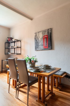 Un coin repas avec une table en bois, des chaises, un vase de fleurs et un tableau représentant une cabine téléphonique rouge accroché au mur.