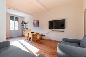 Un salon avec un téléviseur, un coin repas avec des chaises et une table, et un canapé.