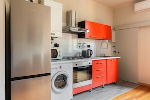 Une cuisine compacte équipée d’un réfrigérateur en acier inoxydable, d’un lave-linge, d’une cuisinière à gaz et de meubles de rangement rouges.