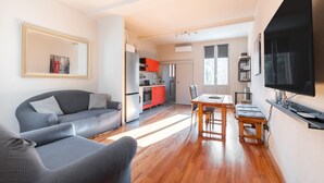 A modern living room with a sofa, a dining table with chairs, a TV mounted on the wall, and a kitchen in the background. - Apartment 'Mirasole House' with Wi-Fi and Air Conditioning (bologna)