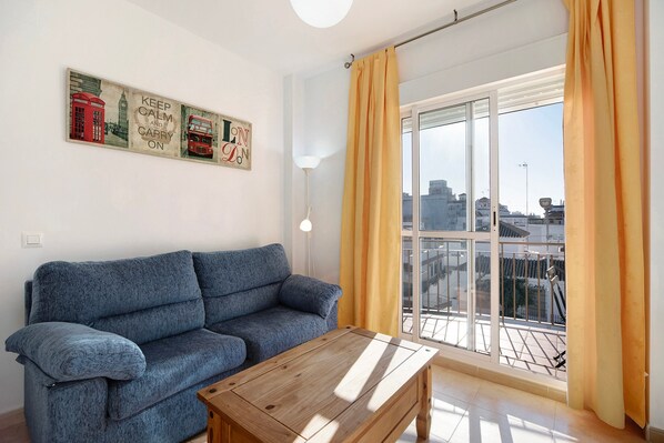 A living room with a sofa, a wooden coffee table, and a cityscape view through a large window with yellow curtains.