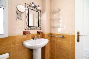 A bathroom with a white sink, a mirror with lights, a towel rack, and a towel dispenser.