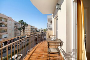 A balcony with a tiled floor, a table with chairs, and a railing overlooking a street with cars and buildings.
