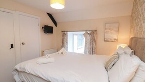 Een slaapkamer met een bed, een televisie aan de muur, een raam met gordijnen en een lamp.