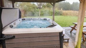 Een hottub onder een houten pergola, met een gazon en een houten omheining op de achtergrond.