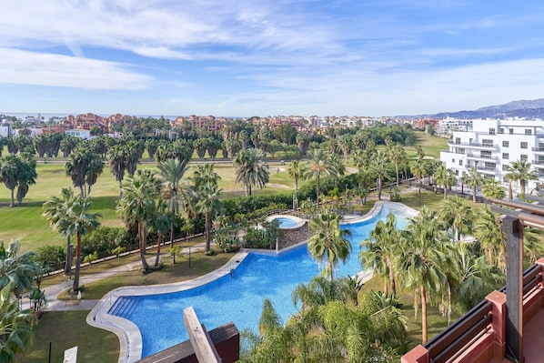 A resort with a swimming pool, palm trees, and a view of the city.