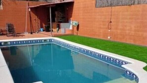 Une piscine dont le bord est recouvert de carrelage, entourée d’une pelouse et d’un mur en briques.