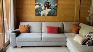 A modern living room with a grey sectional sofa, a painting of a mountain scene, and a wooden ceiling. - Half-chalet facing the Bossons and Taconnaz glaciers (Chamonix Mont Blanc)