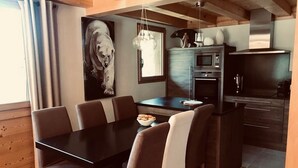 A modern kitchen with a dining area, featuring a black countertop, stainless steel appliances, and a dining table with chairs. - Half-chalet facing the Bossons and Taconnaz glaciers (Chamonix Mont Blanc)