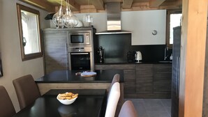 A modern kitchen with a dining area, featuring a built-in oven, microwave, and a large window. - Half-chalet facing the Bossons and Taconnaz glaciers (Chamonix Mont Blanc)