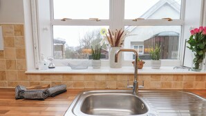 A kitchen with a stainless steel sink, a window above the sink, and various kitchen items on the windowsill. - Manor Farmhouse (Filey)