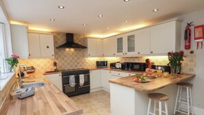A modern kitchen with white cabinets, a wooden countertop, a central island with stools, and a built-in oven. - Manor Farmhouse (Filey)
