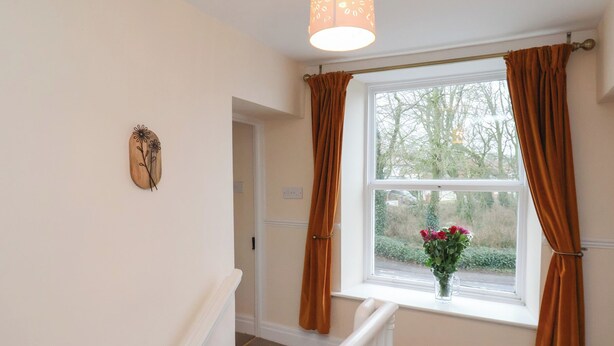 Un escalier avec une rampe blanche, une fenêtre avec des rideaux marron et un luminaire fixé au mur.