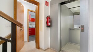 Un pasillo con una puerta de madera, un extintor y un ascensor.