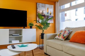 A living room with a sofa, a TV, a plant, and a window.