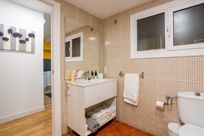A bathroom with a tiled wall, a window, a sink, and a toilet.