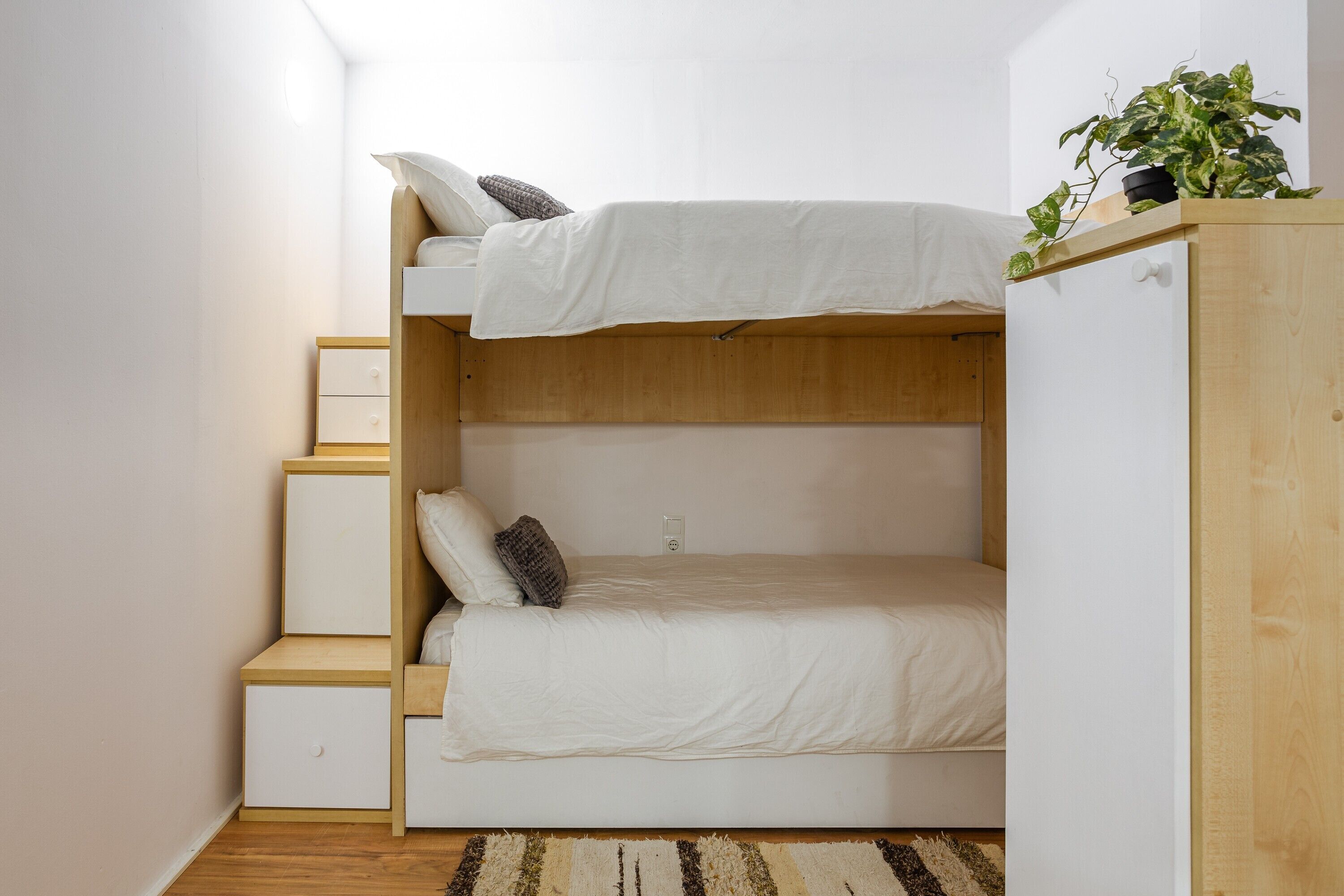 Ein Stockbett mit weißer Matratze, einem Holz-Kopfteil und einer kleinen Pflanze oben drauf.
