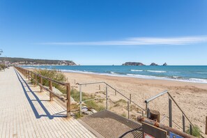 Une promenade en bord de mer, dotée d’une rambarde, qui mène à une plage de sable.